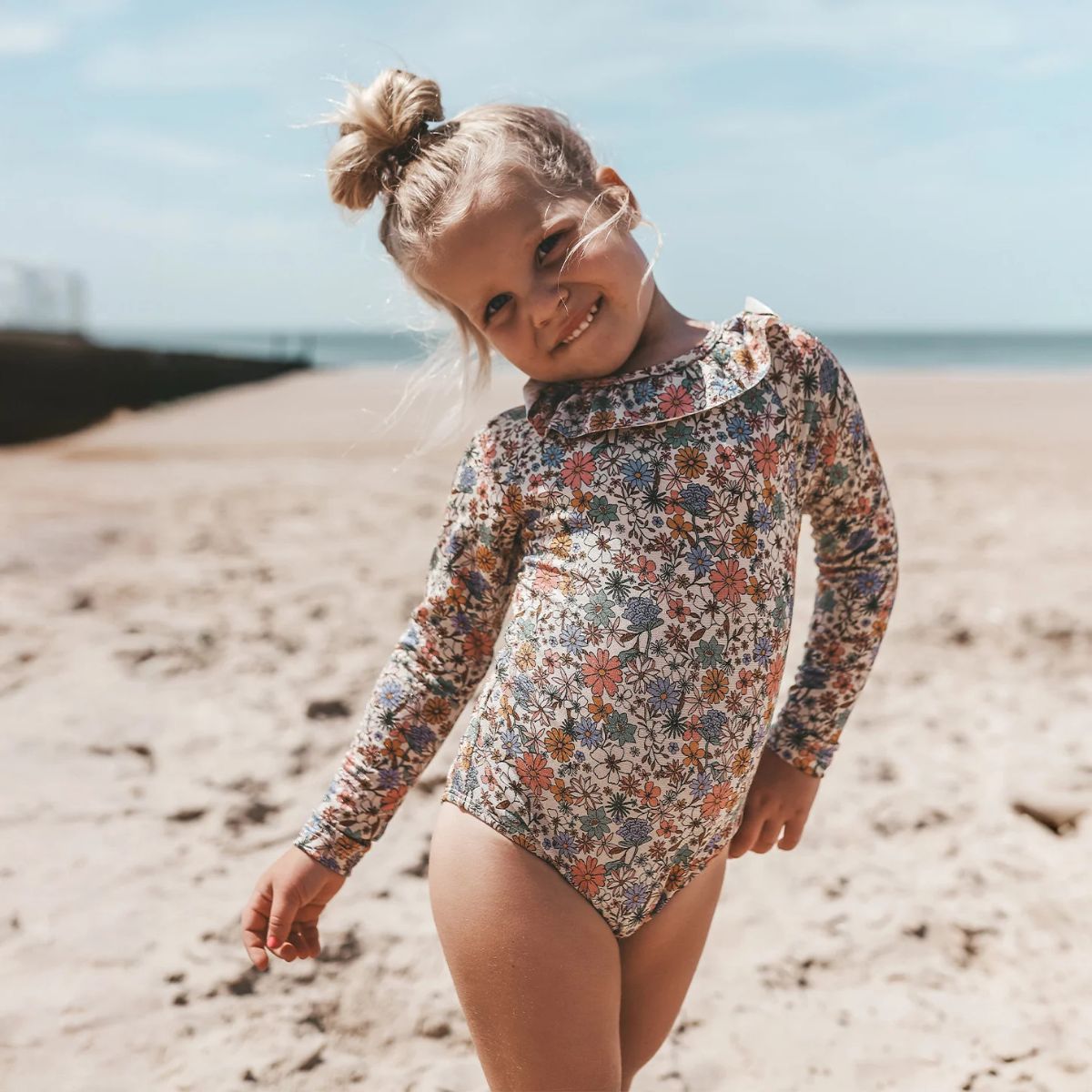 Het Salted Stories sparkly fleurs badpak met lange mouwen beschermt de huid tegen de zon (UPF50+). Het badpak heeft een mooie glitterstof, een print van gekleurde bloemen en ruches aan de bovenkant. VanZus