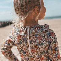Het Salted Stories sparkly fleurs badpak met lange mouwen beschermt de huid tegen de zon (UPF50+). Het badpak heeft een mooie glitterstof, een print van gekleurde bloemen en ruches aan de bovenkant. VanZus
