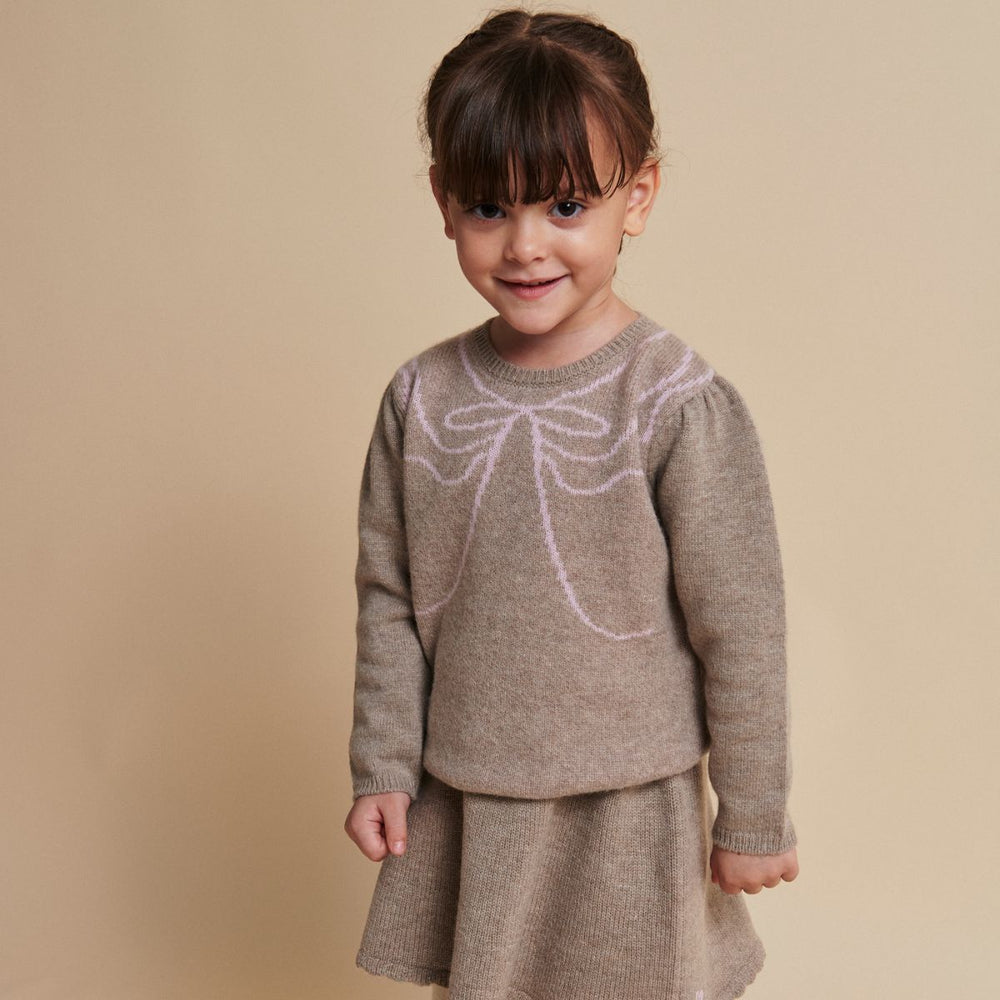 De Copenhagen Colors cashmere bow deco trui sand/bubblegum is een warme trui met een speels accent. De zachte beige kleur vormt een rustige basis, terwijl de roze strik op de borst de trui opvallend maakt. VanZus