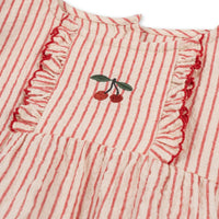 Op zoek naar een schattige romper voor je baby? Dan is de ellie ruches romper amour stripe van Konges Slojd een perfecte keuze.  De gestreepte romper heeft een rode kleur en een print van een kers op de voorzijde. De mouwen en het voorpand zijn afgewerkt met ruches en de romper heeft korte elastische pijpen.