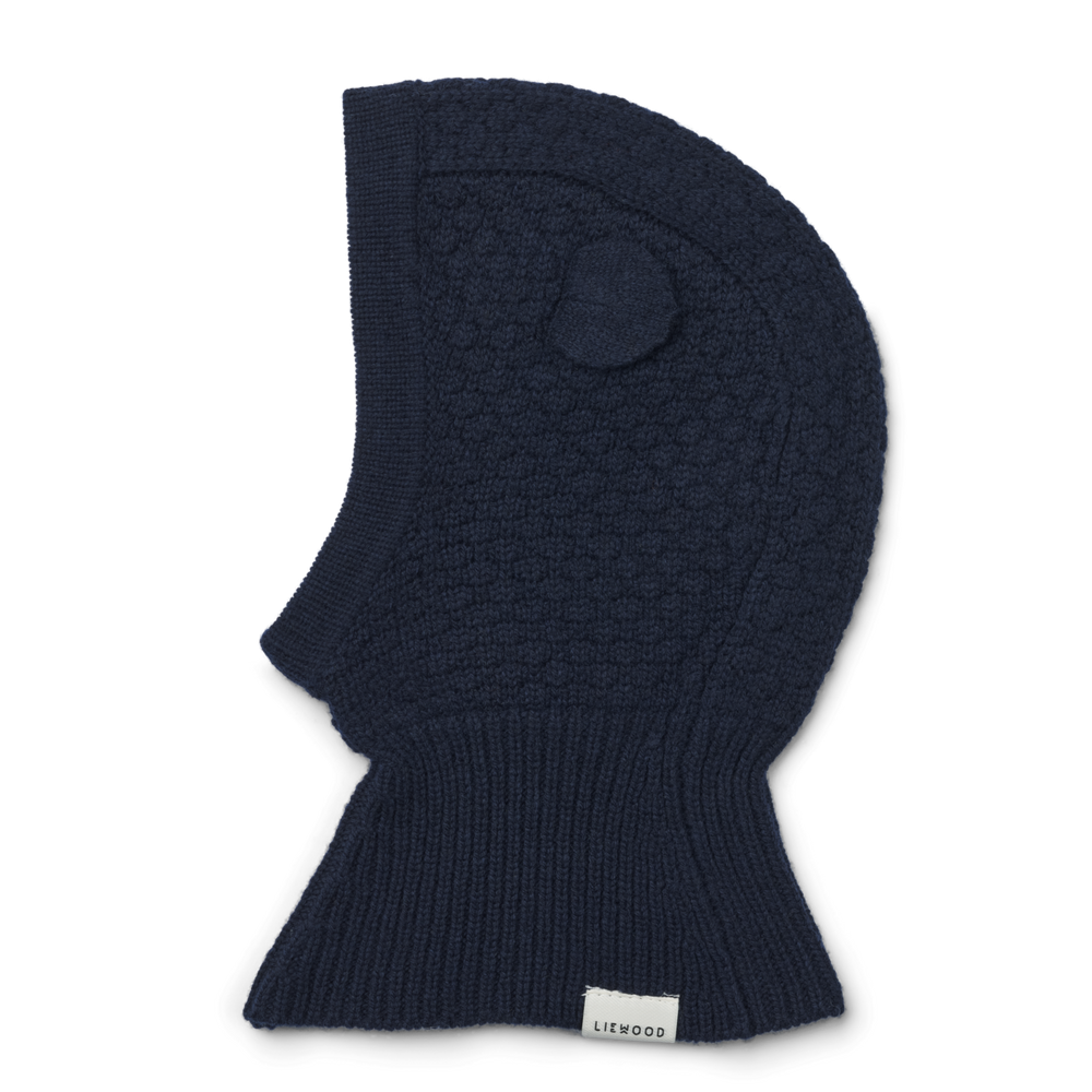 Houd het hoofdje van je kindje lekker warm tijdens de koude wintermaanden met deze oggy balaclava muts in de kleur classic navy van het merk Liewood. Deze zachte en warme muts gaat helemaal om het hoofd van je kleintje heen, waardoor zowel de nek, als het hoofd en de oren lekker warm blijven! VanZus