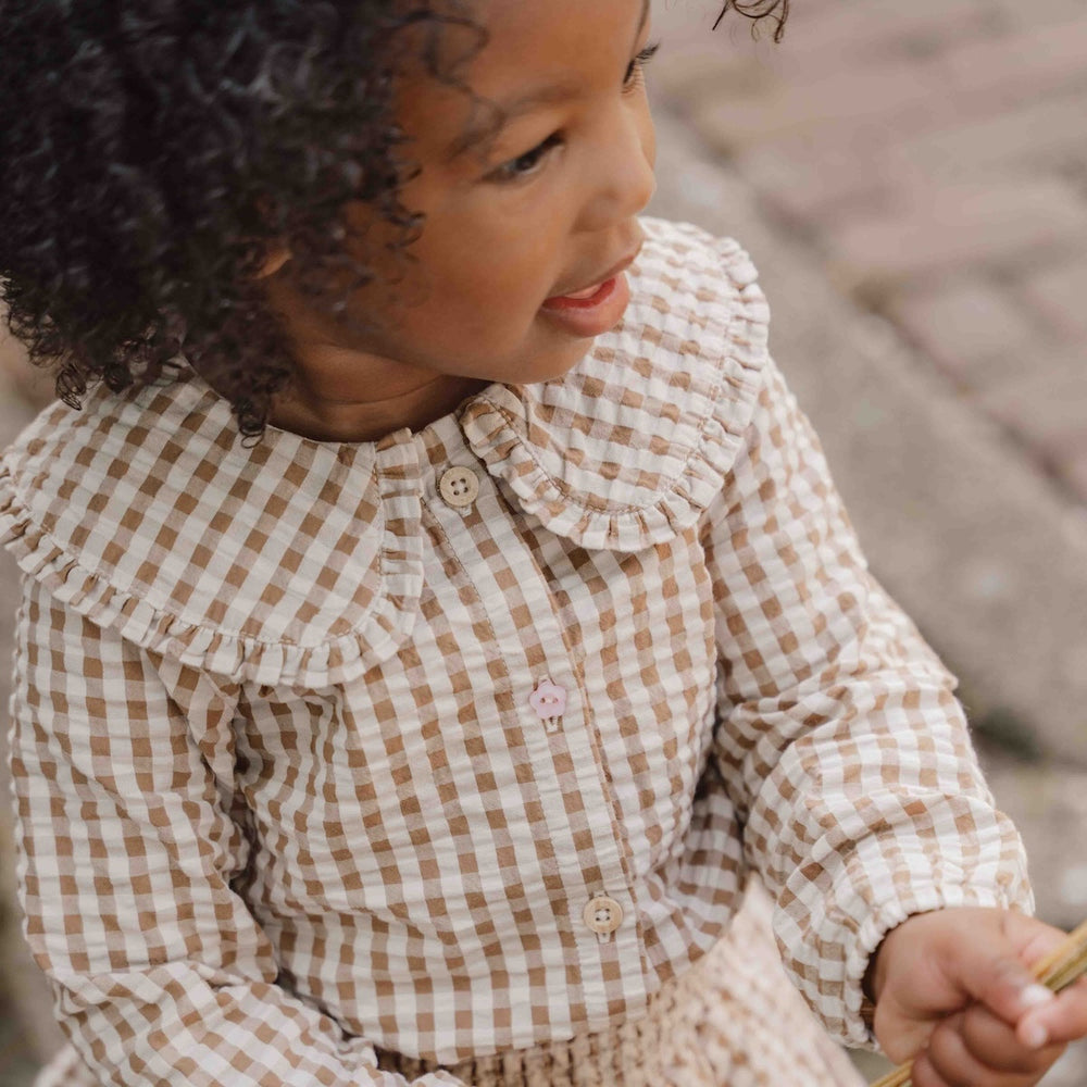 Hoe je de blouse brown check van Little Dutch ook combineert: je meisje zal er geweldig uitzien! De geruite blouse met lange mouwen heeft een bruin-wit patroon en een mooie opvallende kraag met ruches. Zo ziet de blouse er meteen heel bijzonder en meisjesachtig uit. De stof met textuur is van biologisch katoen. VanZus