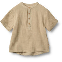 Svend shirt van het merk Wheat in de kleur soft sand: korte mouwen, knoopjes, loose fit, zandkleur en gemaakt van zacht en duurzaam materiaal. Combineer met bijpassende short voor een complete look. VanZus